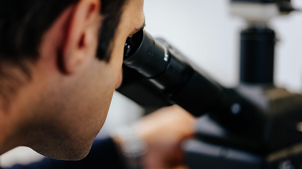 Eine Person blickt durch ein Mikroskop.